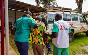 Two MSF medical staff help a patient reach MSF ambulance car in Jansuk Clinic, Yei County, Central Equatoria.