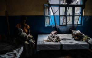 A woman sits with her child in her arms as her youngest son lies in bed while being treated for cholera at the Sake Referral Center, supported by MSF as part of its emergency response. They had to leave the Bulengo displacement camp to come to Sake