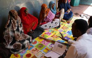 Mothers sit together during a mental health and psychosocial support session led by mental health promoters. Health workers guide discussions on coping with stress and caring for young children after displacement.