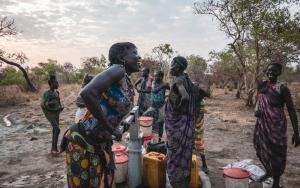 Sera James a resident of Akello village, draws water from the bore hole as she shares a laugh with h