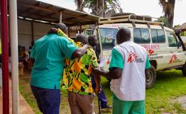 Two MSF medical staff help a patient reach MSF ambulance car in Jansuk Clinic, Yei County, Central Equatoria.