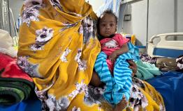 Ferdos holds her 11-month-old baby, Banan, who is infected with measles, in the isolation ward at El Geneina Teaching Hospital, which is supported by MSF. War forced Ferdos and her family to flee to El Geneina, where they live in overcrowded conditions with other families. Her son contracted measles and infected his 11-month-old daughter, who was unvaccinated.