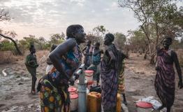 Sera James a resident of Akello village, draws water from the bore hole as she shares a laugh with h