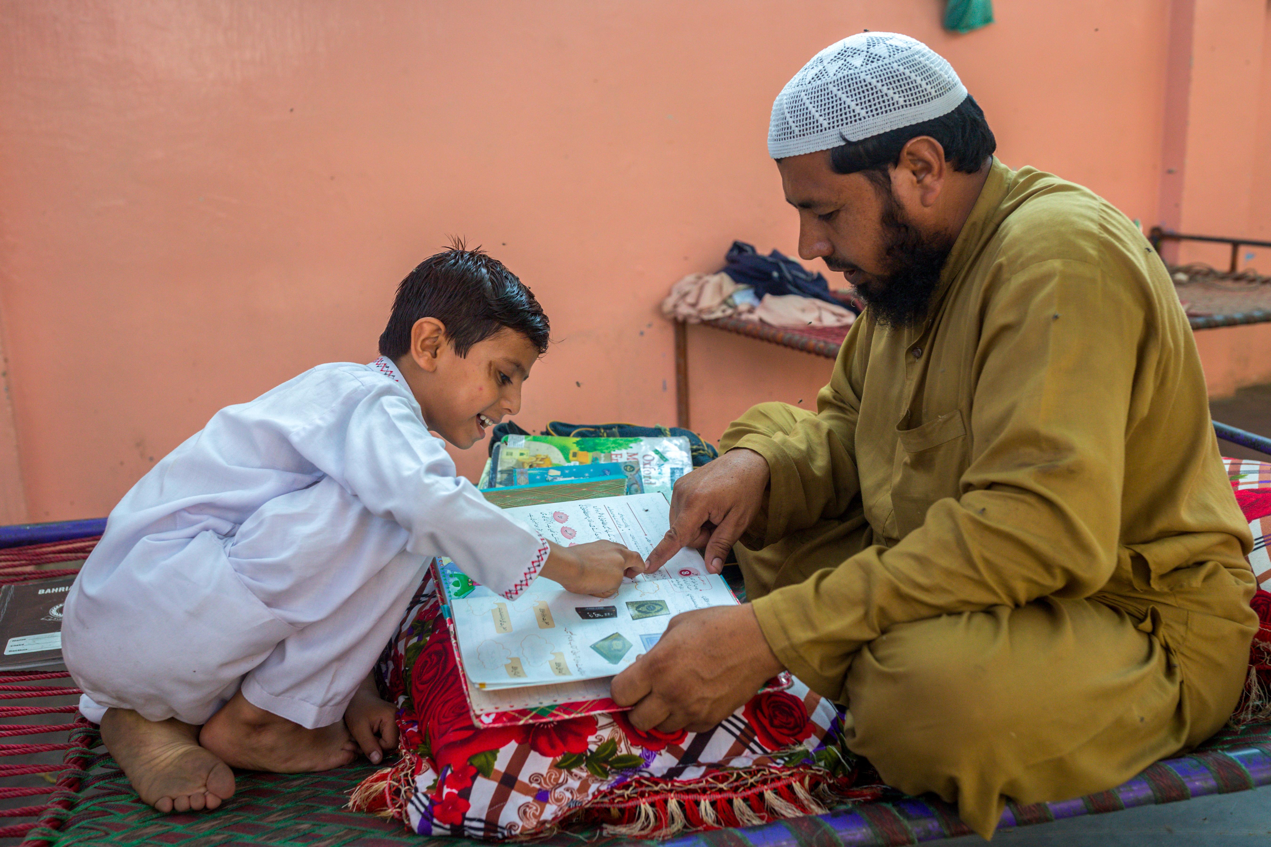 Shahid Khan helps his son, Abdul Rehman, with his homework inside their home in Machar Colony