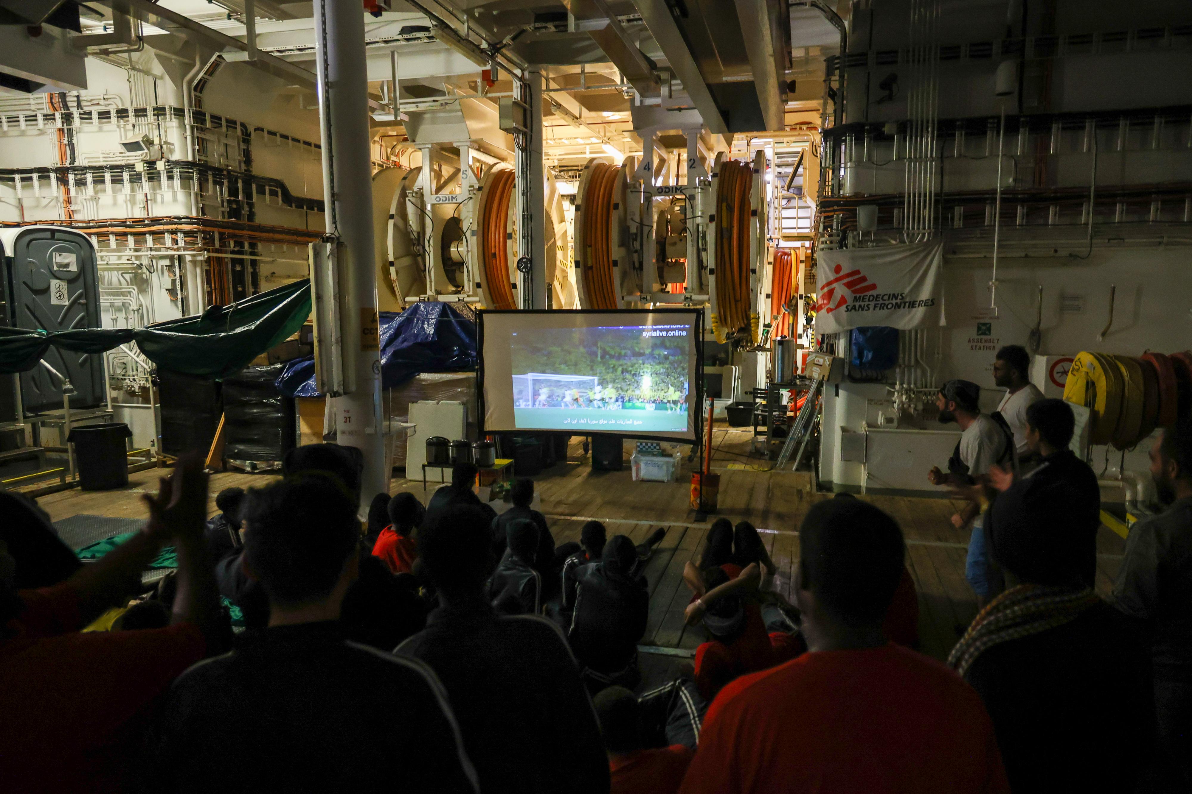 On board the deck of the Geo Barents rescue ship, people gather to watch the football champions league final. 