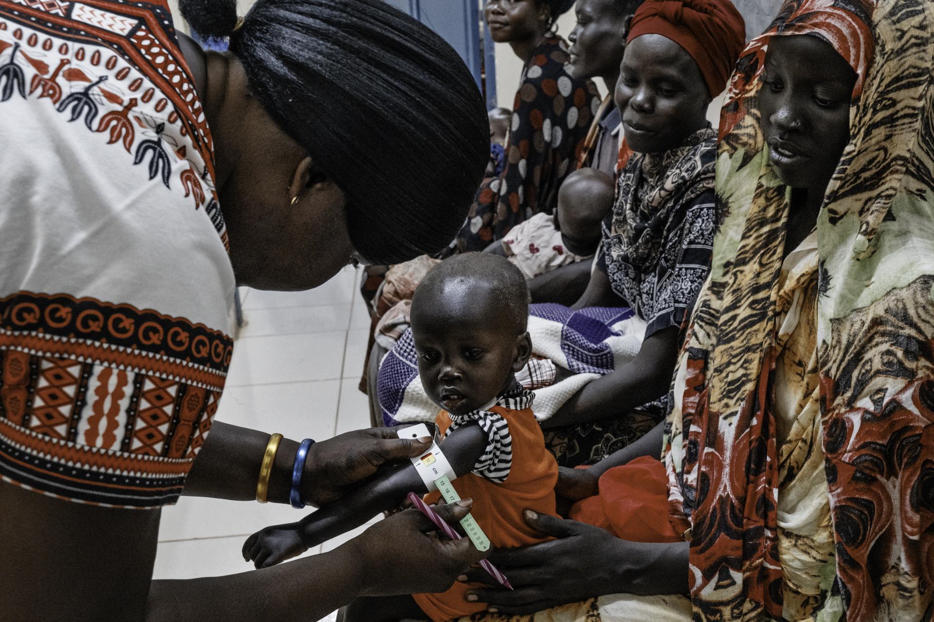 Malnutrition screening of one-year-old Alnel on the knees of his mother Nyanbeny. Ameth Bek Hospital, Abyei.