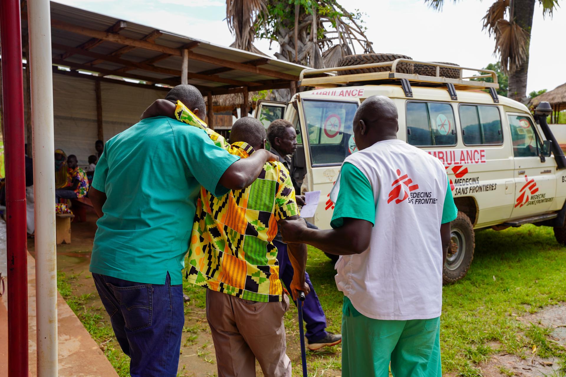 Two MSF medical staff help a patient reach MSF ambulance car in Jansuk Clinic, Yei County, Central Equatoria.