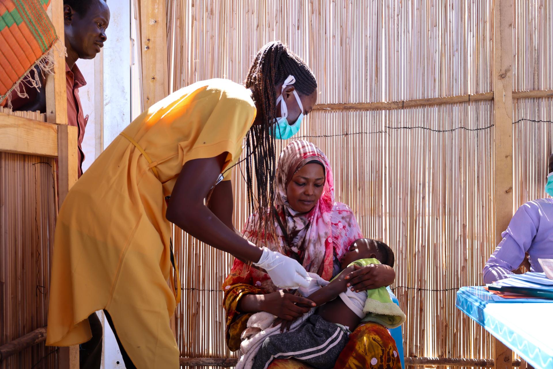 Halima is holding her daughter Aszed during vaccination