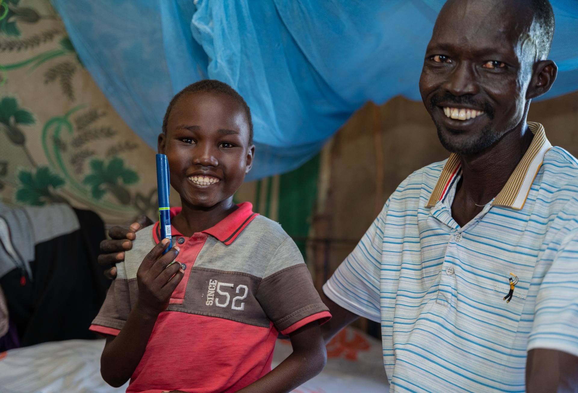 Aher Lual, 11, holds an insulin pen next to his father in their home in Ariath, Aweil North. He prefers the pen to the vial injections he used before.