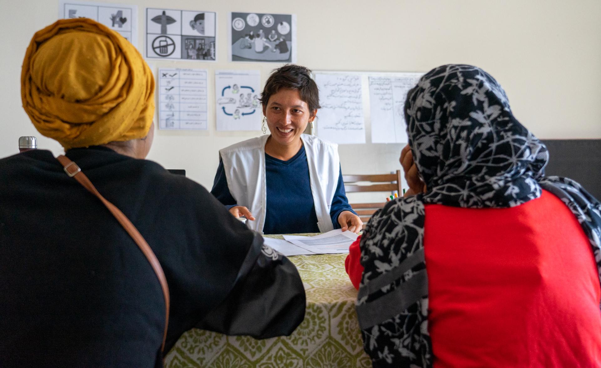 Medium shot of an MSF health promoter speaking to two women during a health promotion consultation at the MSF Sea House Clinic in Lesvos.