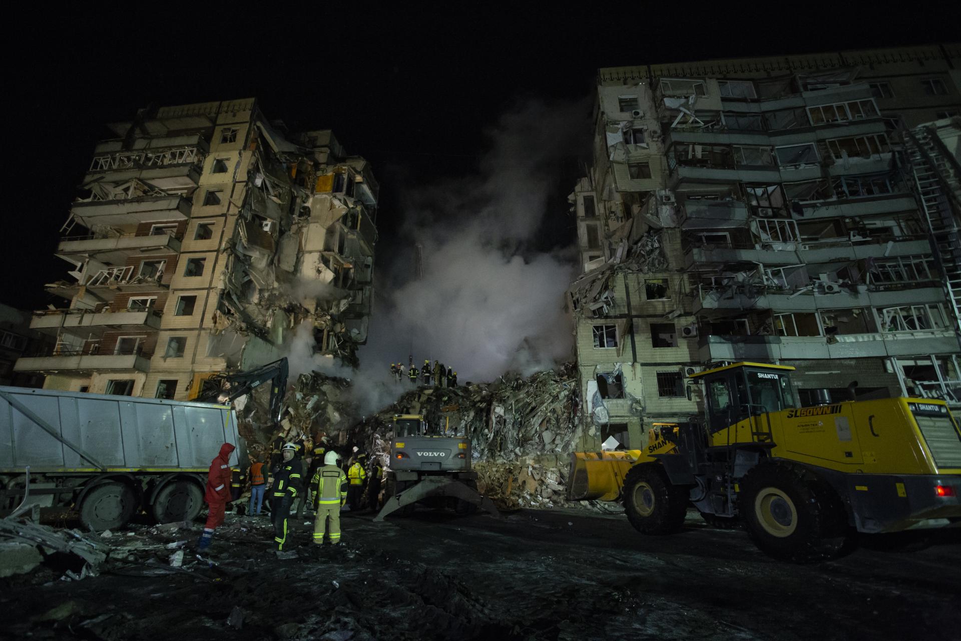 DNIPRO, UKRAINE - JANUARY 15: Firefighters stand near a dump truck while their colleagues are conducting search and rescue operations at residential building hit by a missile on January 15, 2023 in Dnipro, Ukraine.