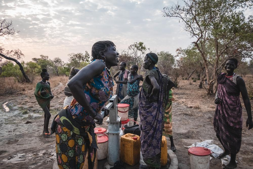 Sera James a resident of Akello village, draws water from the bore hole as she shares a laugh with h