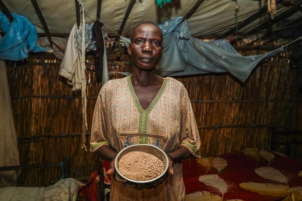 Elizabeth Nyakuony James holds a bowl of sorghum in her makeshift shelter made of flood-damaged wood and plastic bags.