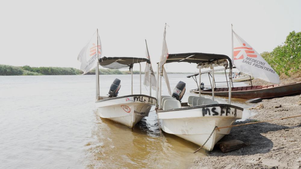 MSF medical boat crossing the Sobat River in South Sudan, with flags displaying the Médecins Sans Frontières logo fluttering in the wind.