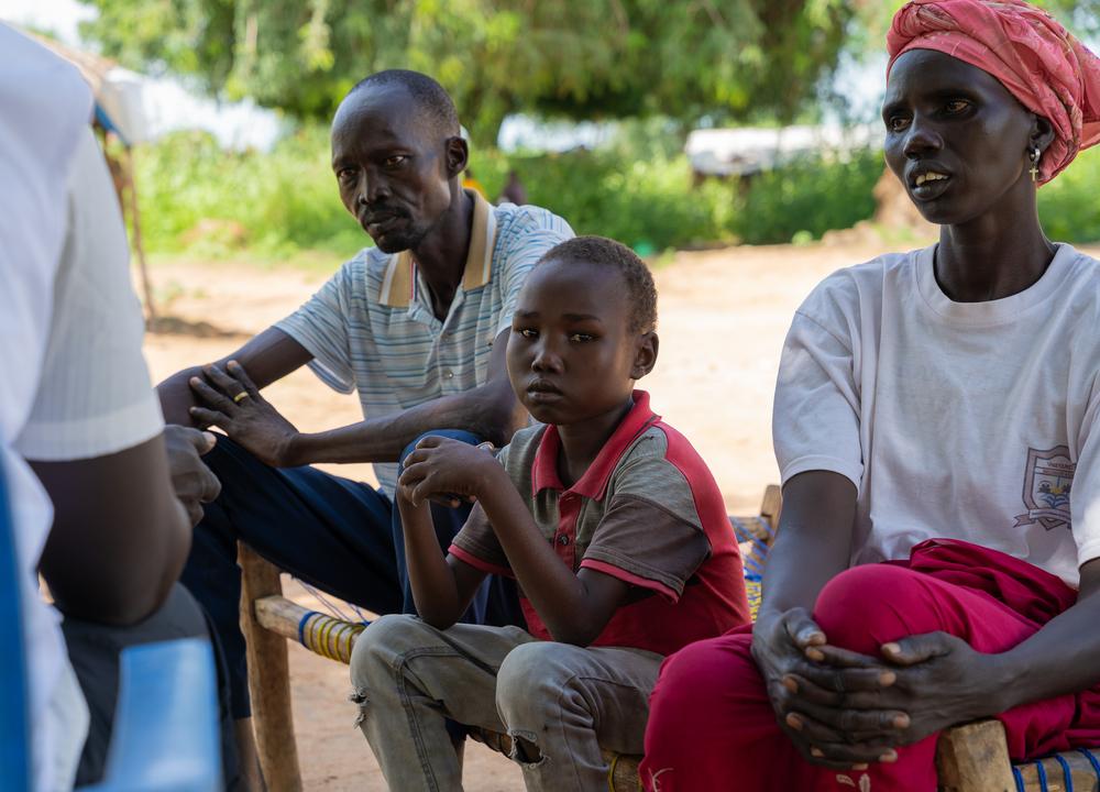 Aher Lual, 11, sits with his family at their home in Arith, Aweil North. Their are speaking MSF staff