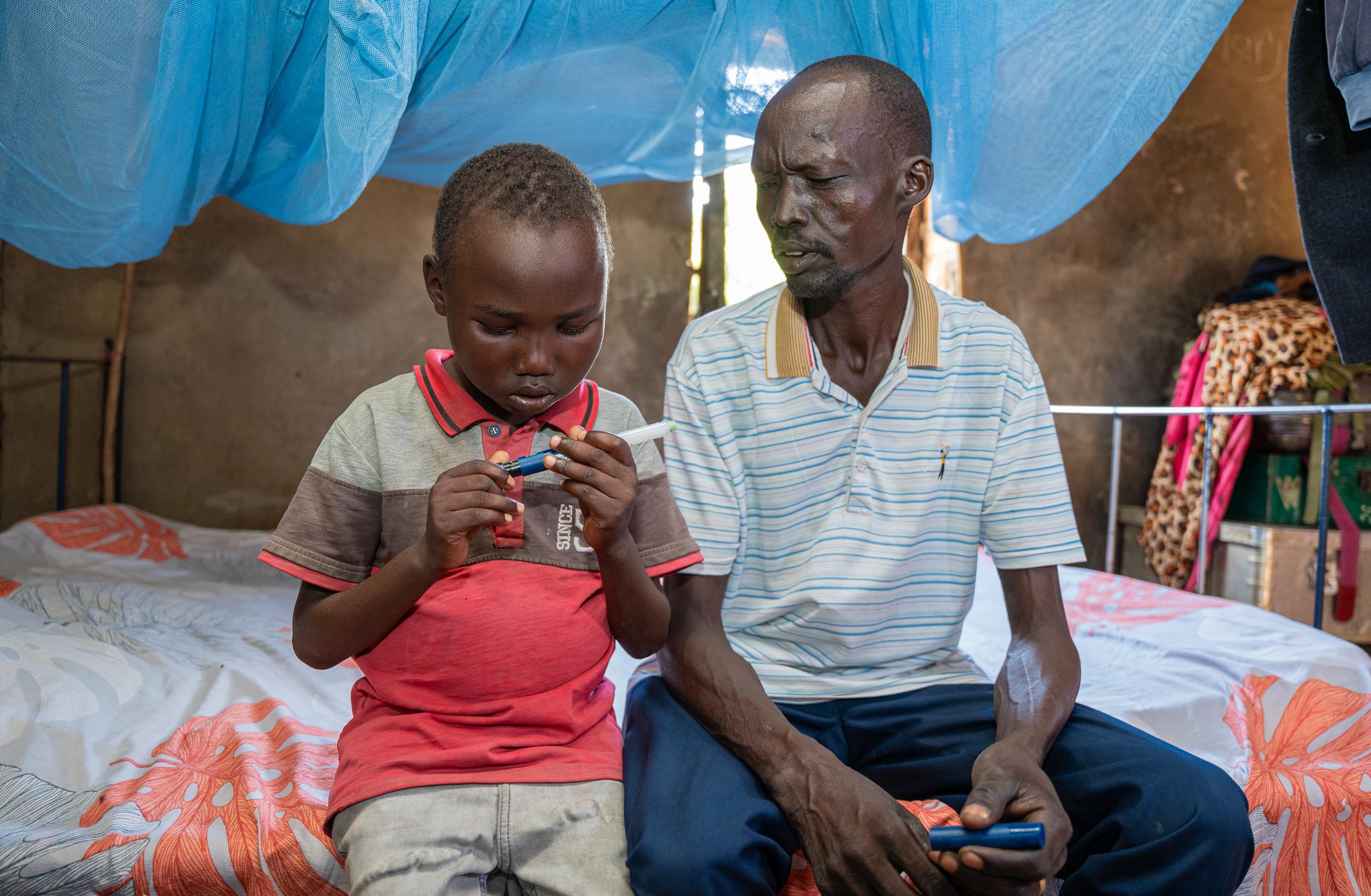 Aher Lual, 11, demonstrates to his father how to use the insulin pen. A skill he first learned from him.
