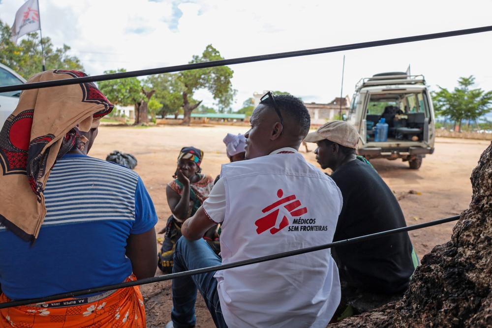 MSF staff Amade José chats with a group of displaced people below a tree, just outside an MSF mobile clinic in Alua Sede, Eráti District, Nampula Province.