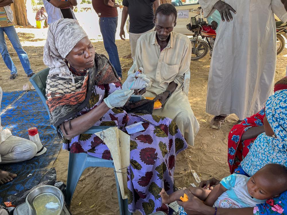 A vaccination officer in Allerye, Chad, administering a diphtheria vaccine to a mother and her young son.