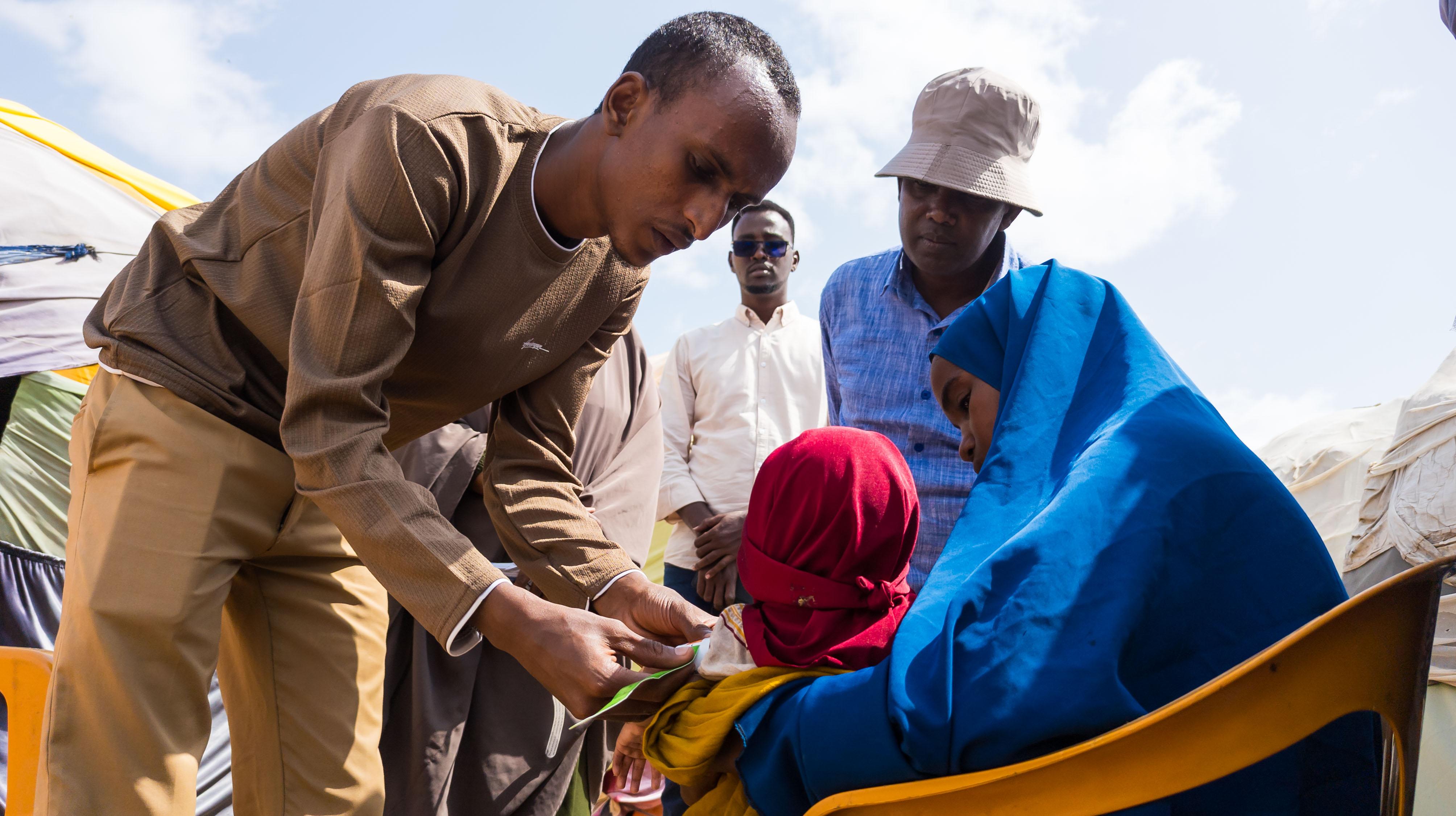 Mohamud Moktar, a community health worker measures a child's mid-upper arm circumference (MUAC) at an internally displaced persons (IDP) site in Baidoa, Somalia. The measurement is part of a cluster-wide assessment to screen for malnutrition among displaced mothers and children in IDPs of Baidoa.